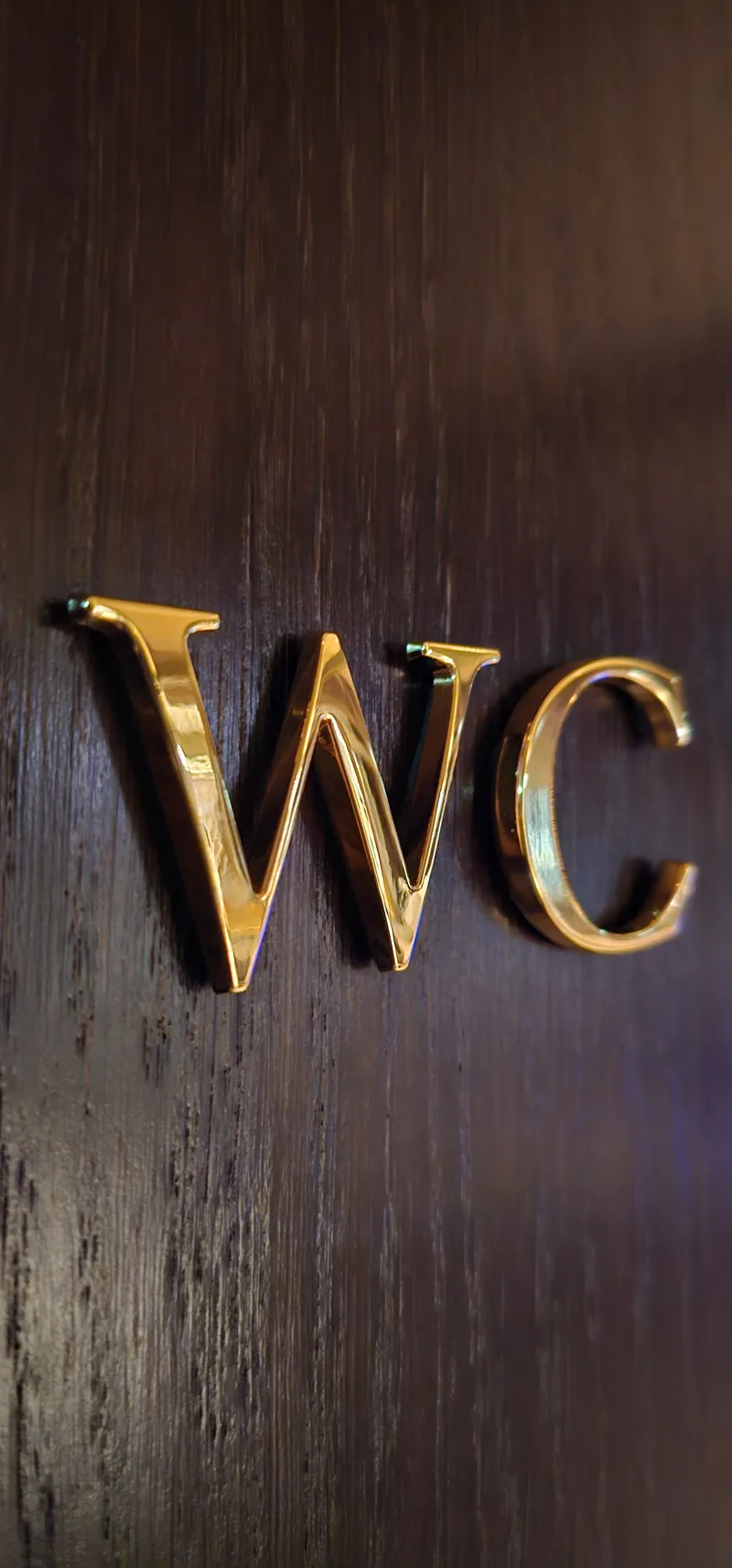 Gullhúðaðir WC-stafir á dökkri viðarhurð